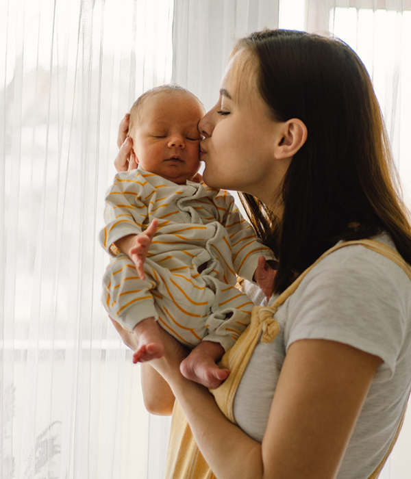 Mother playing with newborn baby son at home near the window. Happy infant and mom. Pregnancy help near Hastings MN