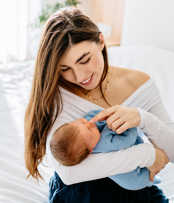 Mother gently holding newborn baby on sunlit bed